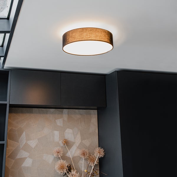 Moderne runde Deckenleuchte mit braunem Stoffschirm, montiert an weißer Decke über dunklen Schränken in einem organisierten Raum.