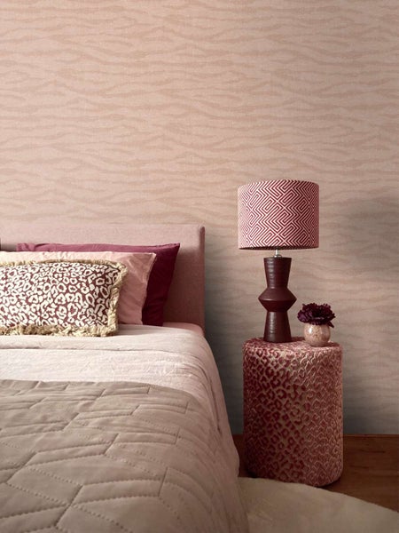 Modernes Schlafzimmer mit gemusterter Tapete mit Wellenstruktur, Bett mit Textilkissen und Nachttisch mit Tischlampe und Blumendekor
