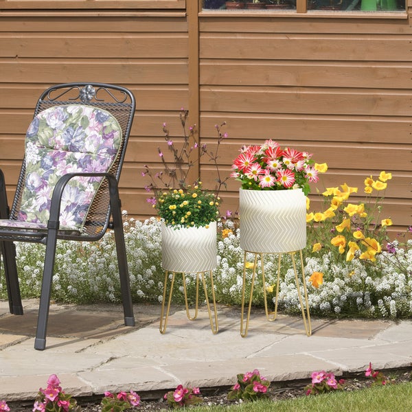 Gartenszene mit zwei Pflanzgefäßen auf goldenen Gestellen und einem Stuhl mit floralem Kissen