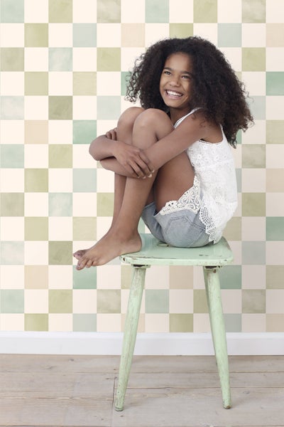 Mädchen sitzt auf einem Hocker vor einer Wand mit Schachbrettmuster