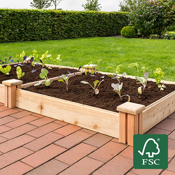 Zwei Hochbeete aus FSC-zertifiziertem Holz mit Gemüsepflanzen auf einer gepflasterten Terrasse vor einem Garten mit Rasen und Hecke.