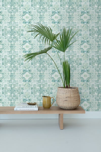 Dekorative Tapete mit abstraktem Muster im Wohnraum mit Pflanze, Karaffe und Büchern auf einem Holztisch