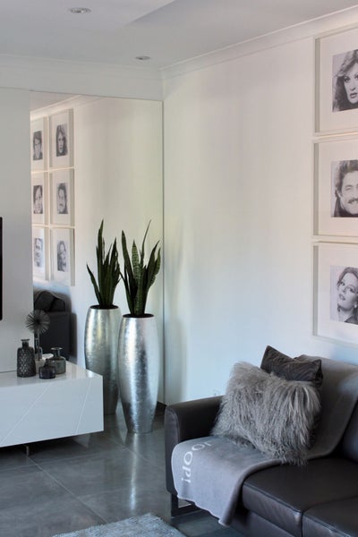 Moderner Wohnraum mit hohen silbernen Bodenvasen und Bogenhanf, großem Wandspiegel sowie einem grauen Sofa mit Dekokissen.