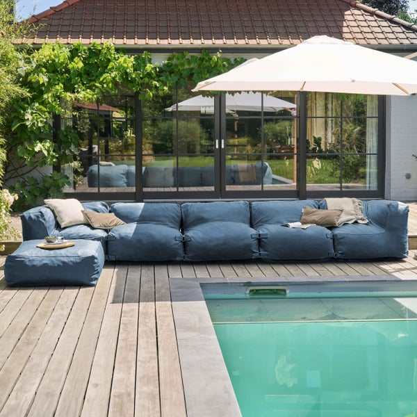 Modulares Outdoor-Lounge-Sofa mit Hocker auf einer Holzterrasse neben einem Swimmingpool, großzügige und helle Gestaltung des Außenbereichs.