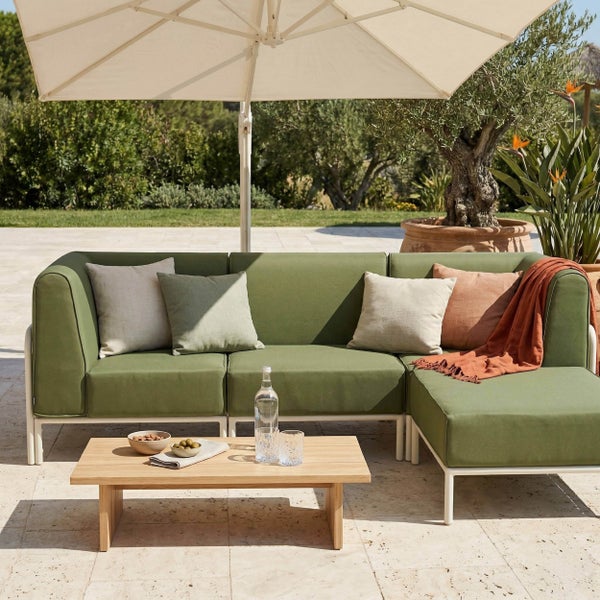 Moderne Gartenlounge mit grünem Ecksofa, hellem Holztisch und großem Sonnenschirm auf einer hellen Terrasse.