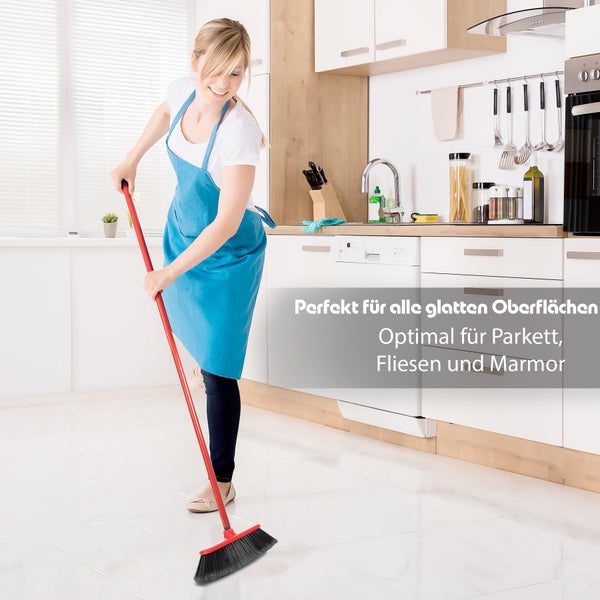 Frau wischt mit einem Besen in einer Küche.