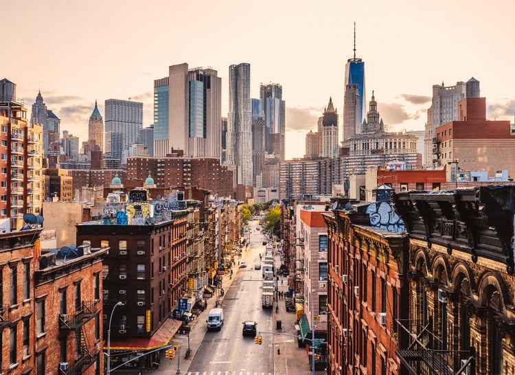 Stadtlandschaft von New York City mit Backsteingebäuden und einer Skyline aus Wolkenkratzern in warmem Abendlicht.