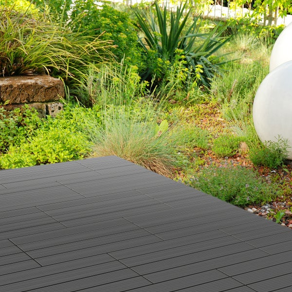 Dunkelgraue WPC Terrassenfliesen verlegt in einem hellen Garten mit Gräsern, Stauden und dekorativen weißen Kugelleuchten.