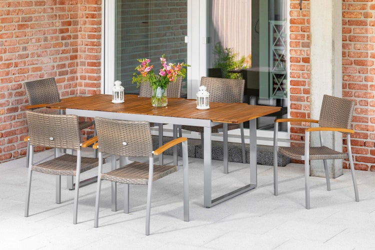 Garten-Essgruppe mit Holztisch auf Metallgestell und Geflechtstühlen auf einer Terrasse vor einer Backsteinwand.