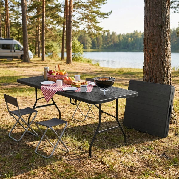 Schwarzer Camping-Klapptisch mit Klappstühlen und Hockern am See, gedeckt mit Picknick und kompaktem Grill für den Außenbereich.