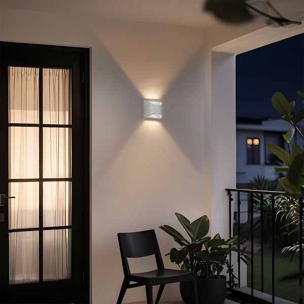 Moderne weiße Wandaußenleuchte auf einer Terrasse bei Nacht, Lichtkegel nach oben und unten, neben einer Tür und einem schwarzen Stuhl.