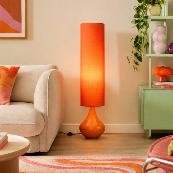 Moderne Stehleuchte mit zylindrischem Stoffschirm und bauchigem Sockel in einem Wohnzimmer mit Sofa und Regal