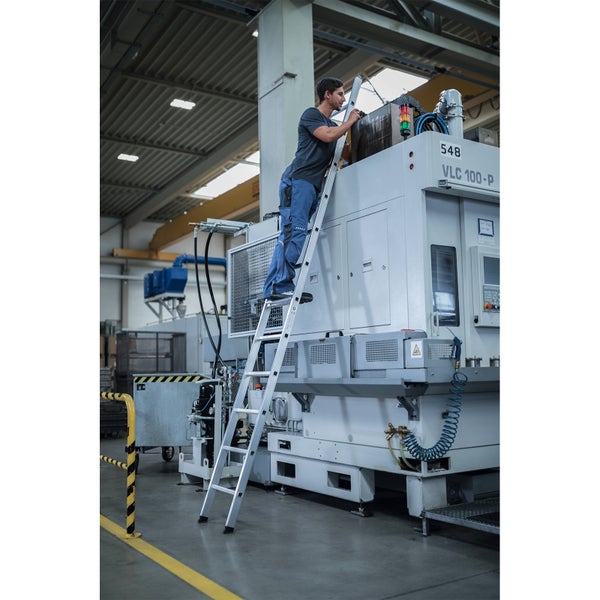 Eine Person benutzt eine Mehrzweckleiter in einer Fabrik, um an einer Maschine zu arbeiten.