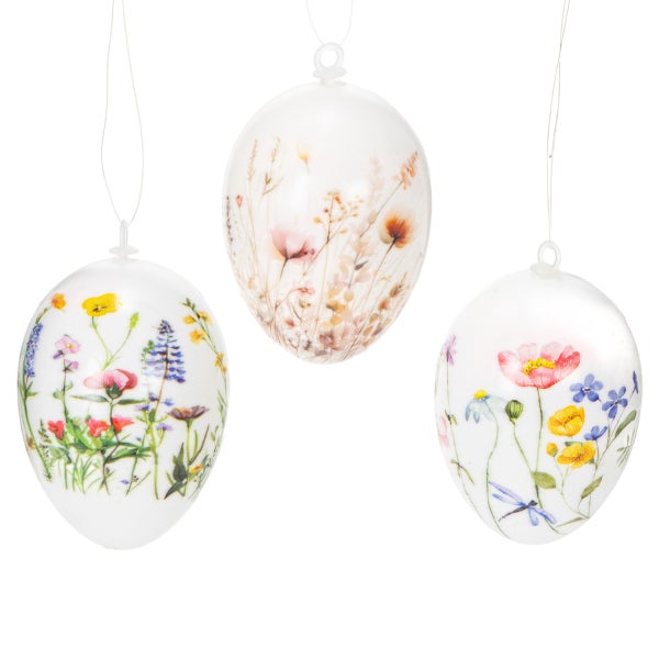 Drei Ostereier aus Glas mit Blumenmotiven hängen an transparenten Fäden