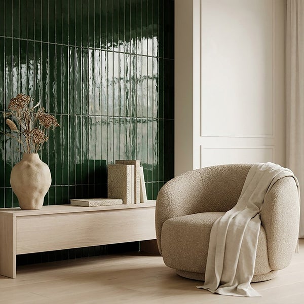Wohnzimmer mit vertikal verlegten, glänzenden Wandfliesen im Format Riemchen, davor helles Sideboard, Sessel mit Boucle Bezug und Dekoration.