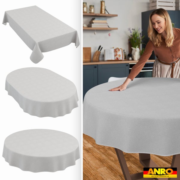 Hellgraue Tischdecke in rechteckiger, ovaler und runder Form. Frau breitet runde Decke auf Küchentisch aus. ANRO Deutsche Manufaktur Logo.