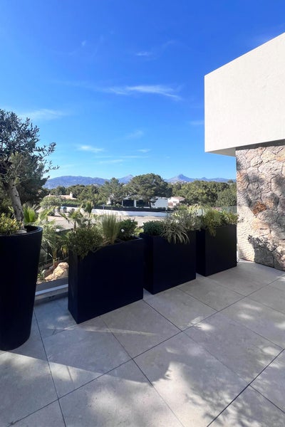 Moderne Terrasse mit großen, schwarzen, rechteckigen Pflanzkübeln als Raumteiler auf Fliesenboden mit Blick in die Natur.
