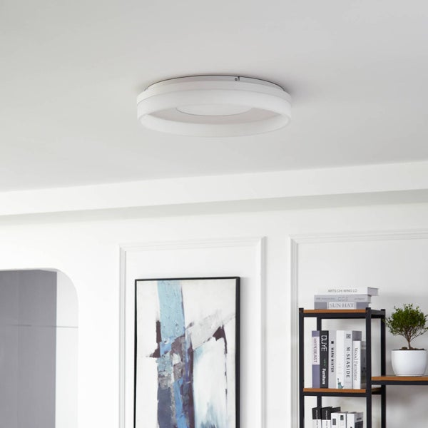 Moderne, runde Deckenleuchte in einem hellen Wohnraum mit Wandbild und Regal.