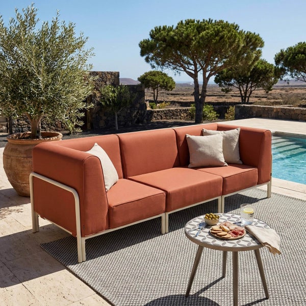 Moderner Outdoor-Loungebereich mit einem terracottafarbenen Dreisitzer-Sofa, einem runden Beistelltisch und einem Teppich neben einem Pool.