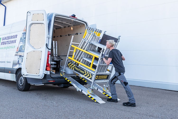 Ein Mann schiebt ein Gerüst mit Hilfe einer Rampe aus einem Lieferwagen.