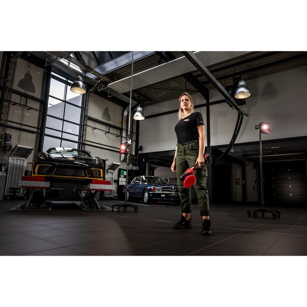 Eine Frau hält eine Akku Poliermaschine in einer professionellen Werkstatt mit Autos auf Hebebühnen und mobilen LED Stativleuchten.