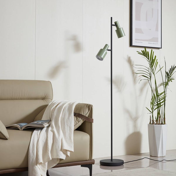 Eine Stehlampe mit zwei Strahlern, einem Sofa, einer Zimmerpflanze und einem Poster in einem Wohnzimmer.