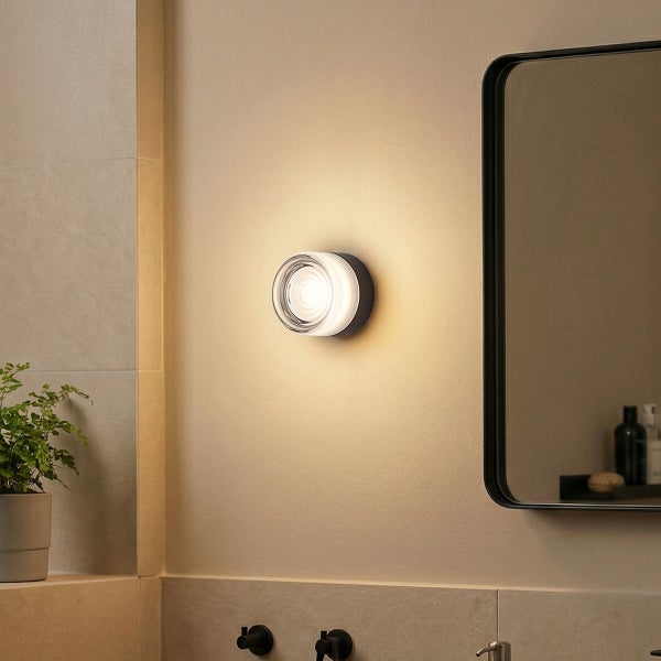 Moderne Wandleuchte in runder Form mit warmem Lichtschein montiert in einem Badezimmer neben einem Spiegel.
