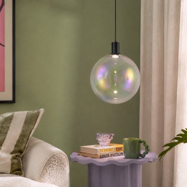 Moderne Pendelleuchte mit einer großen, irisierenden Glaskugel in einem Wohnzimmer mit Beistelltisch und Dekoration.