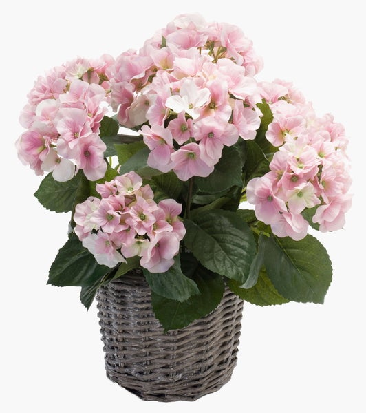 Künstliche Hortensie mit rosa Blüten und grünen Blättern im grauen geflochtenen Korb.