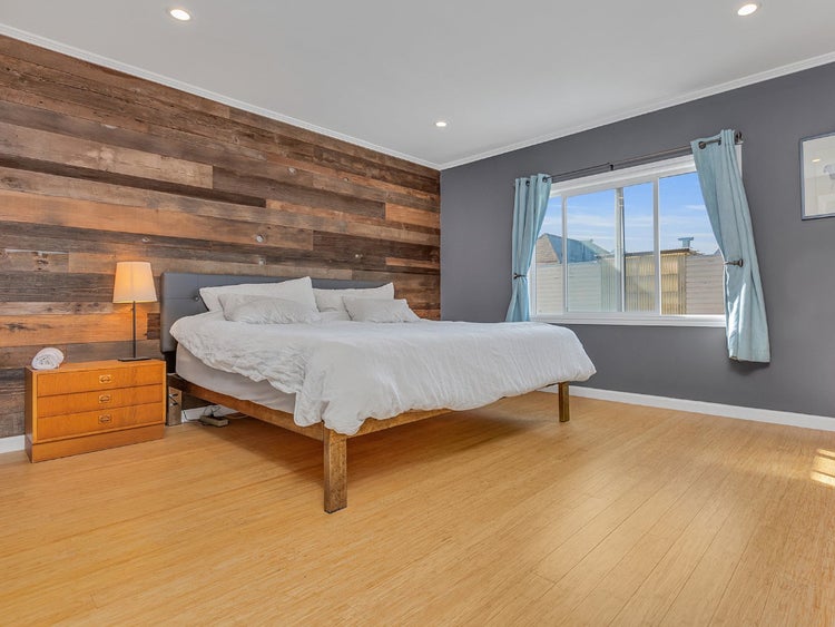 Helles und geräumiges Schlafzimmer mit Akzentwand aus Holzplanken, Doppelbett, Holzboden und Fenster mit Vorhängen.