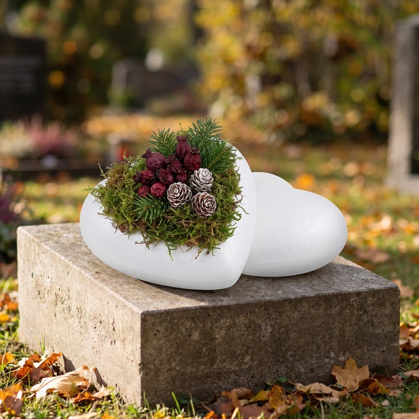 Grabschmuck in Herzform aus Styropor mit Moos und Zapfen auf einem Stein
