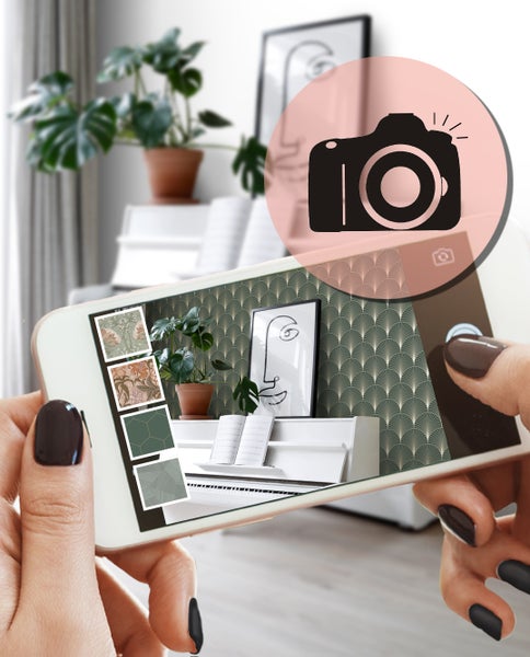 Eine Person hält ein Smartphone, auf dem eine Visualisierung von verschiedenen Tapeten in einem Wohnraum dargestellt wird.