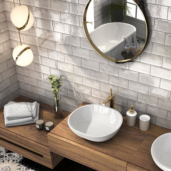 Modernes Badezimmer mit Waschtischplatte aus Holz, Aufsatzwaschbecken, goldener Armatur, runden Spiegeln und glänzenden Wandfliesen im Ziegelformat.