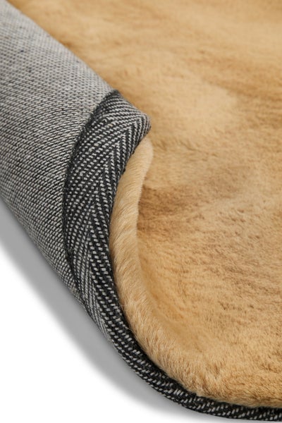 Nahaufnahme eines beigen Teppichs aus Kunstfell mit umgeknickter Ecke und gewebter Rückseite.