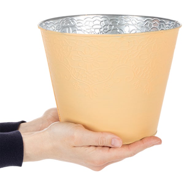 Dekorativer aprikotfarbener Übertopf aus Metall mit floraler Prägung, zur Größenveranschaulichung in den Händen gehalten.