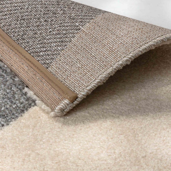 Nahaufnahme eines Teppichs mit gewebtem Rücken, verstärkter Kante und weicher Florstruktur.