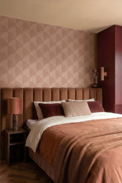 Schlafzimmer mit geometrisch gemusterter Tapete, gepolstertem Kopfteil, Bett mit Strickdecke und Nachttischlampe.