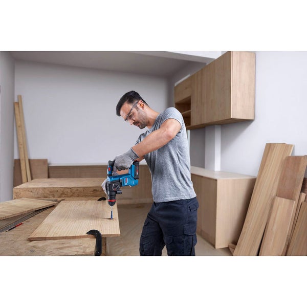 Ein Mann bohrt mit einer blauen Bohrmaschine ein Loch in ein Holzbrett.