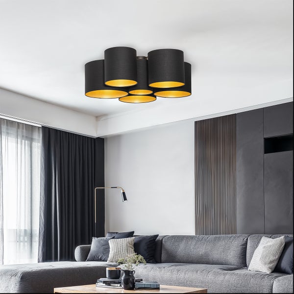 Moderne Deckenleuchte mit sechs zylindrischen Stoffschirmen in Schwarz und Gold in einem modern eingerichteten Wohnzimmer mit grauem Sofa.