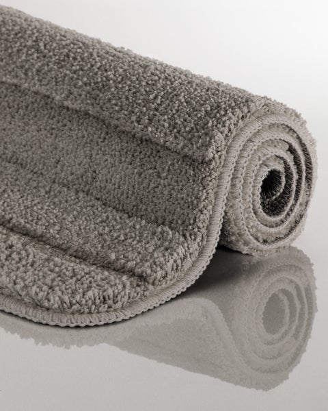 Grauer, flauschiger Badeteppich, teilweise aufgerollt.