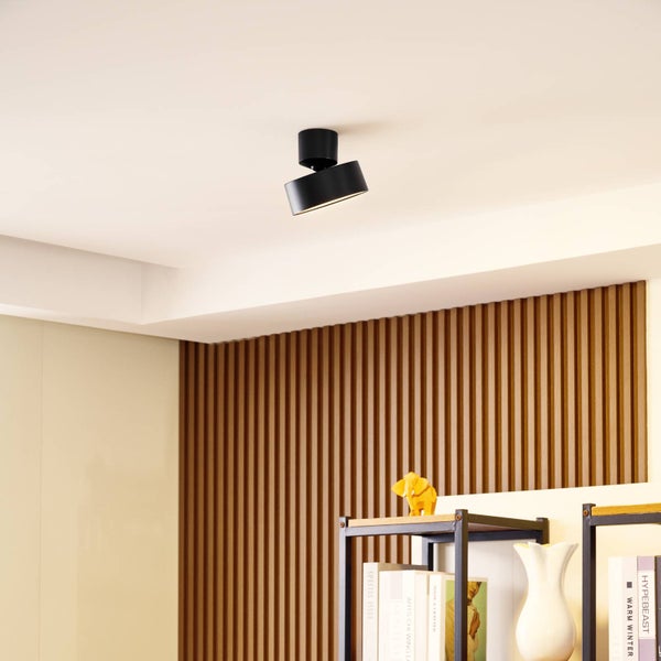 Moderner schwarzer verstellbarer Deckenstrahler an einer Decke in einem Raum mit Holzlamellenwand und einem Regal.
