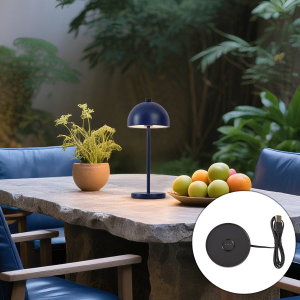 Blaue kabellose LED Tischleuchte auf einem Steintisch im Garten mit Pflanze, Obstschale und einer Ladestation.
