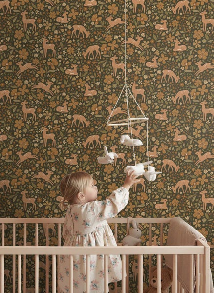 Kind im Kinderzimmer vor einer Vliestapete mit Waldmuster mit Rehen und Blumen in einer gemütlichen und hellen Wohnatmosphäre.