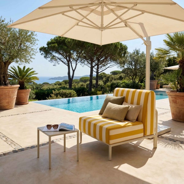 Gelb-weiß gestreifter Garten-Loungesessel mit Beistelltisch unter einem Sonnenschirm auf einer Terrasse am Pool.