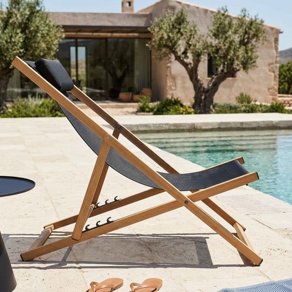 Verstellbarer Liegestuhl aus Holz mit Kopfkissen auf einer hellen Terrasse am Pool, im Hintergrund Olivenbäume und ein Haus.