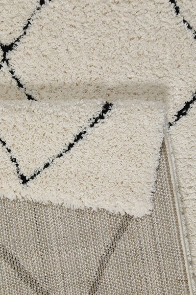 Cremefarbener Hochflor-Teppich mit schwarzem Rautenmuster und gewebter Rückseite.