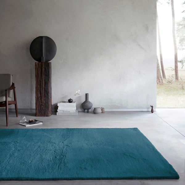 Moderner türkiser Teppich in einem hellen, minimalistischen Wohnzimmer mit grauem Boden und strukturierter Wand.