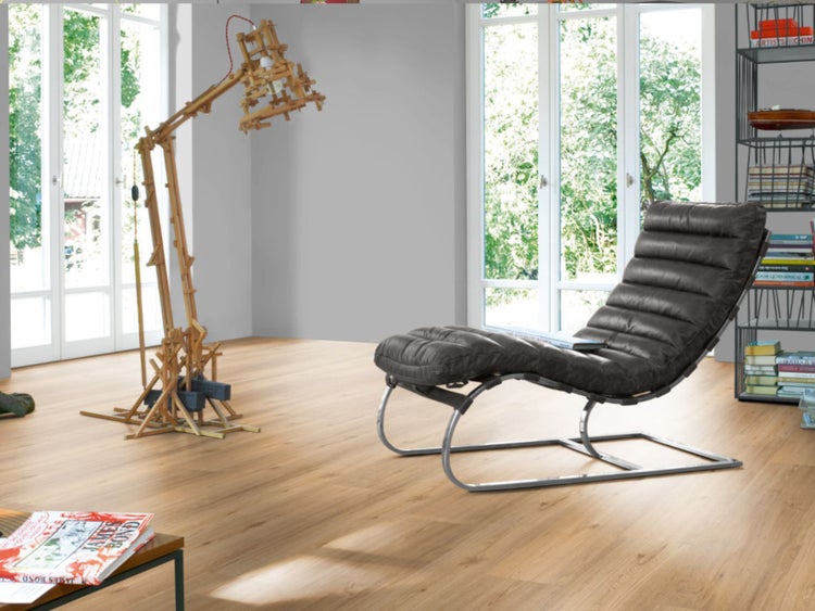 Ein helles, geräumiges Wohnzimmer mit Eichen-Laminatboden, einem modernen anthrazitfarbenen Relaxsessel und einer großen Stehleuchte aus Holzlatten.