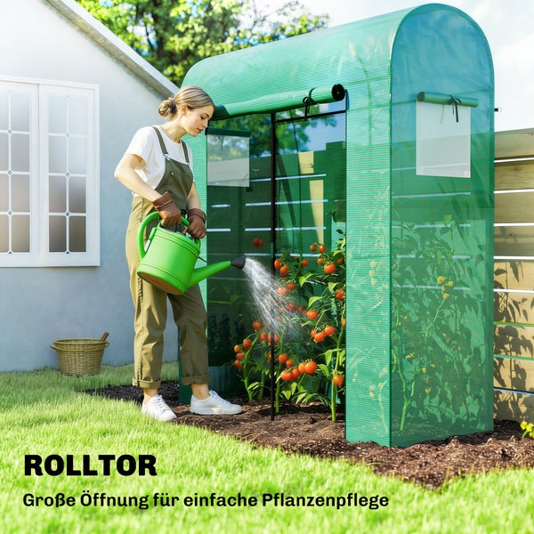 Ein Folien-Gewächshaus mit geöffnetem Rolltor in einem hellen Garten, in dem eine Frau Tomatenpflanzen gießt.