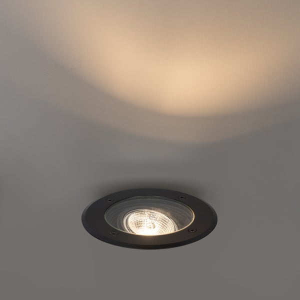 Runder Bodeneinbaustrahler aus Metall mit eingeschaltetem Leuchtmittel und warmem Lichtkegel auf einer Fläche.